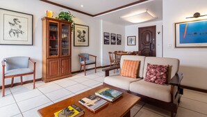Un salon comprenant un canapé, des fauteuils, une table basse avec des livres, un meuble avec des portes en verre et des tableaux encadrés accrochés aux murs.