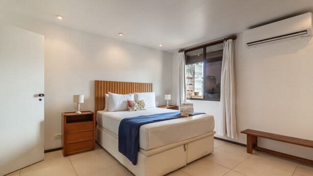 Une chambre d’hôtel moderne avec un grand lit, des tables de chevet, un banc et une fenêtre avec des rideaux.