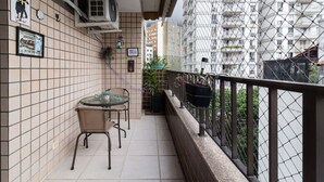 Un balcon aux murs recouverts de carreaux, une table avec des chaises, des plantes en pot et une vue sur un immeuble de grande hauteur.