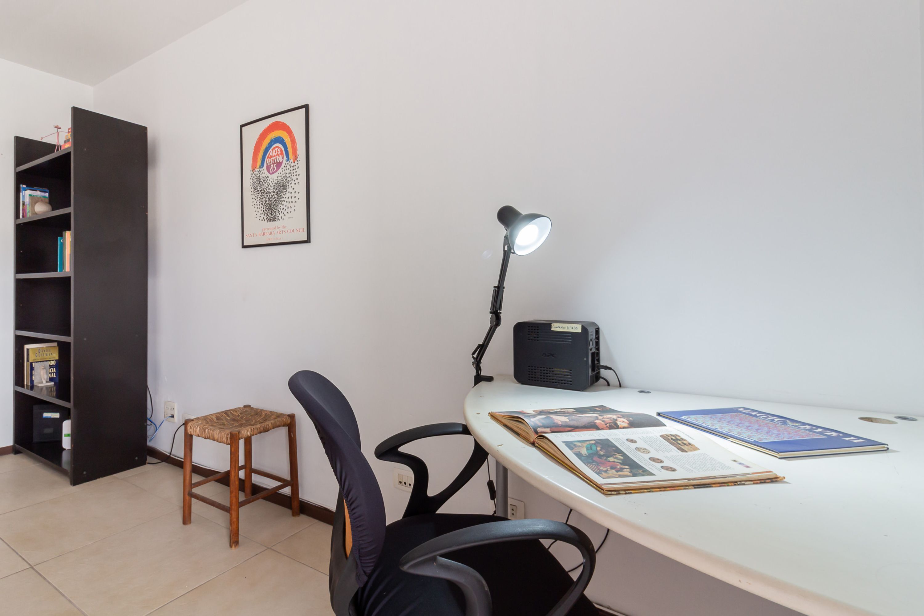 Un espacio de estudio con escritorio, dos sillas, una lámpara, una estantería y un cuadro en la pared.