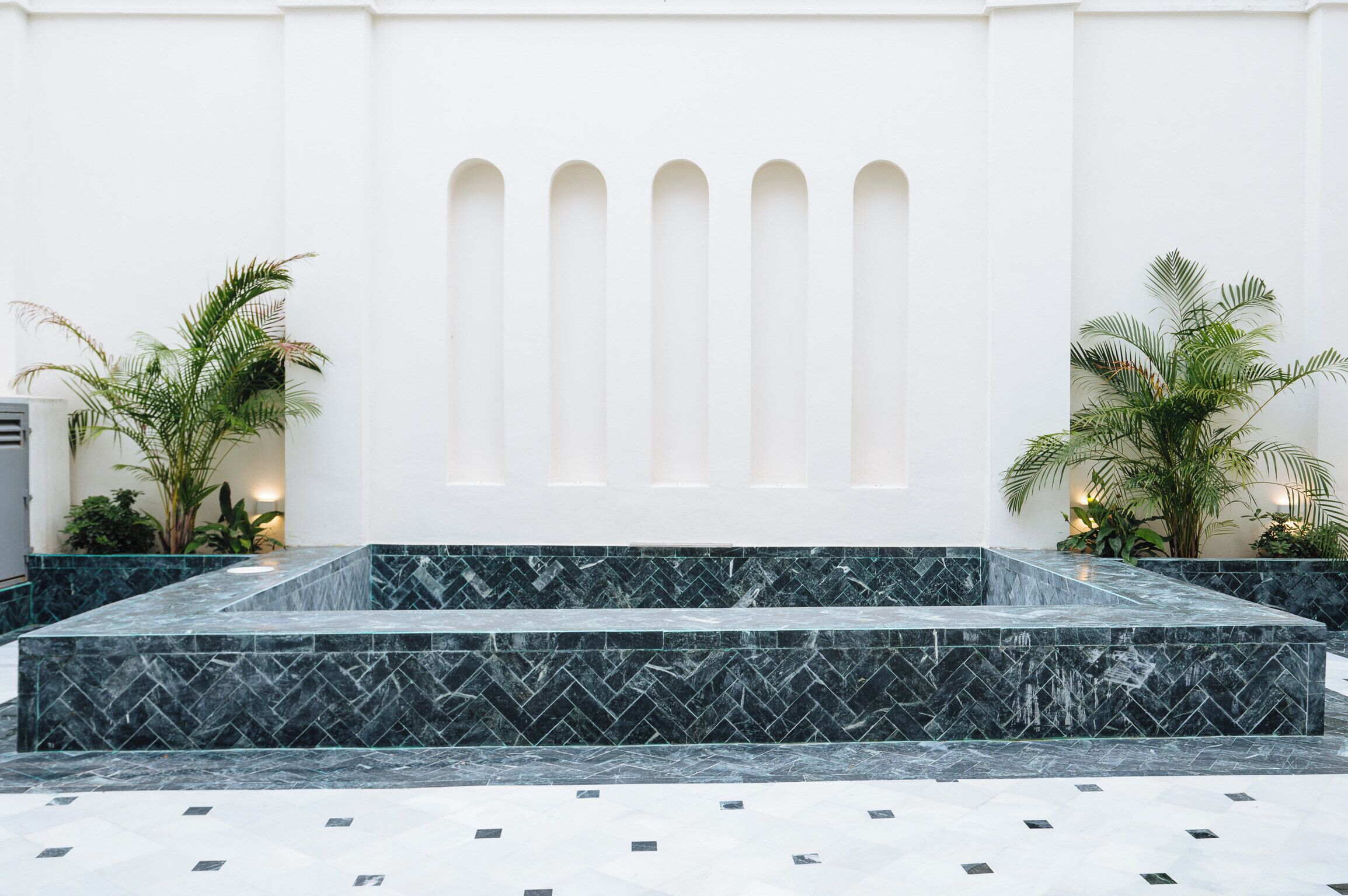 Um hall moderno com uma escadaria de mármore, paredes brancas e plantas em vasos.