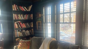 A cozy living room with a sofa, pillows, a bookshelf, and a window with blinds.