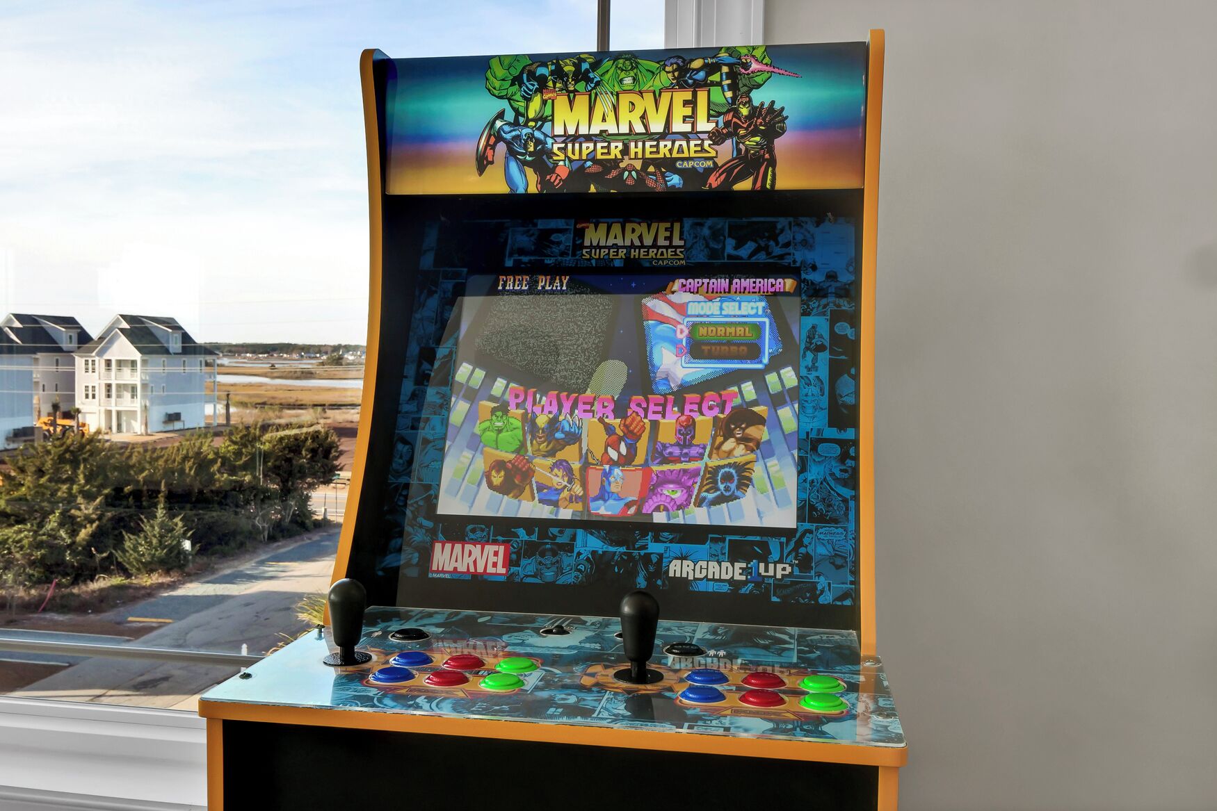 Une borne d’arcade Marvel Super Heroes avec une vue sur des maisons et une route à l’extérieur.