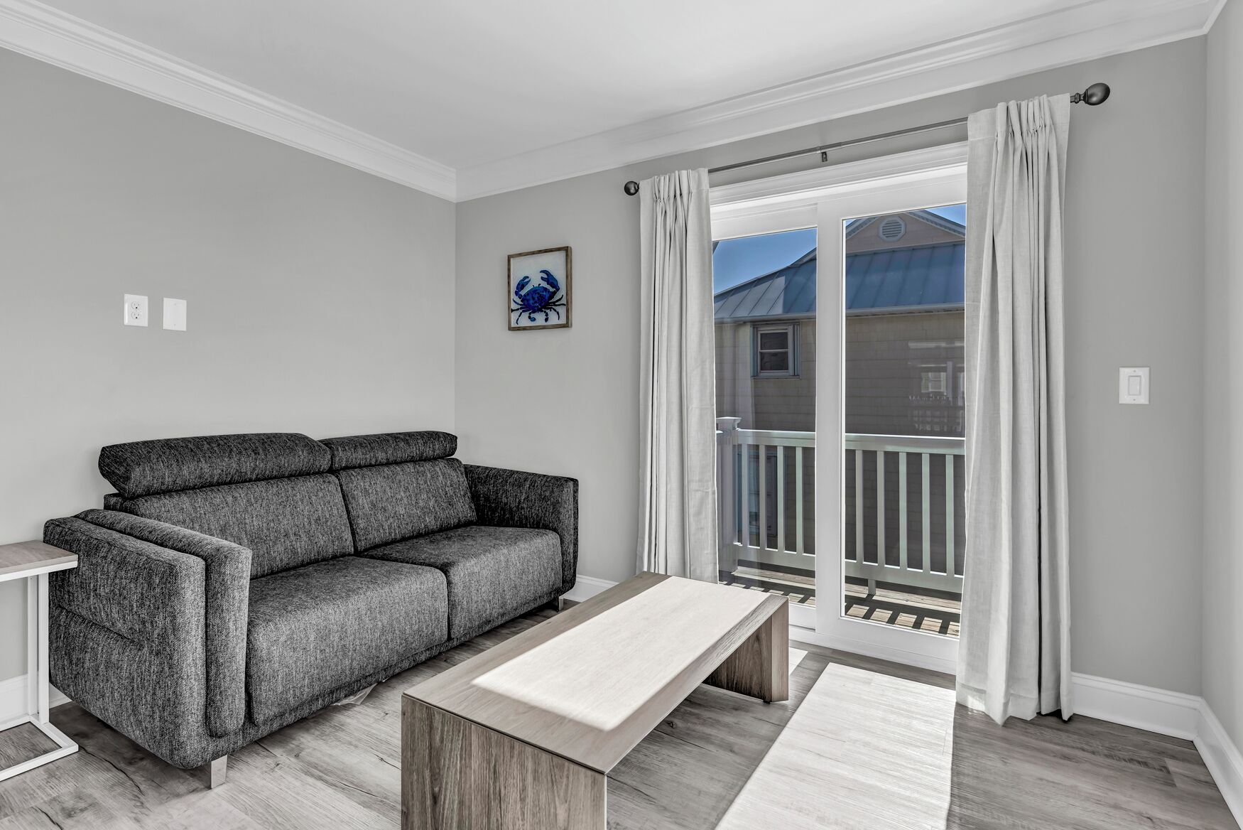 Un salon moderne avec un canapé gris, une table basse en bois et une porte-fenêtre coulissante donnant sur un balcon.