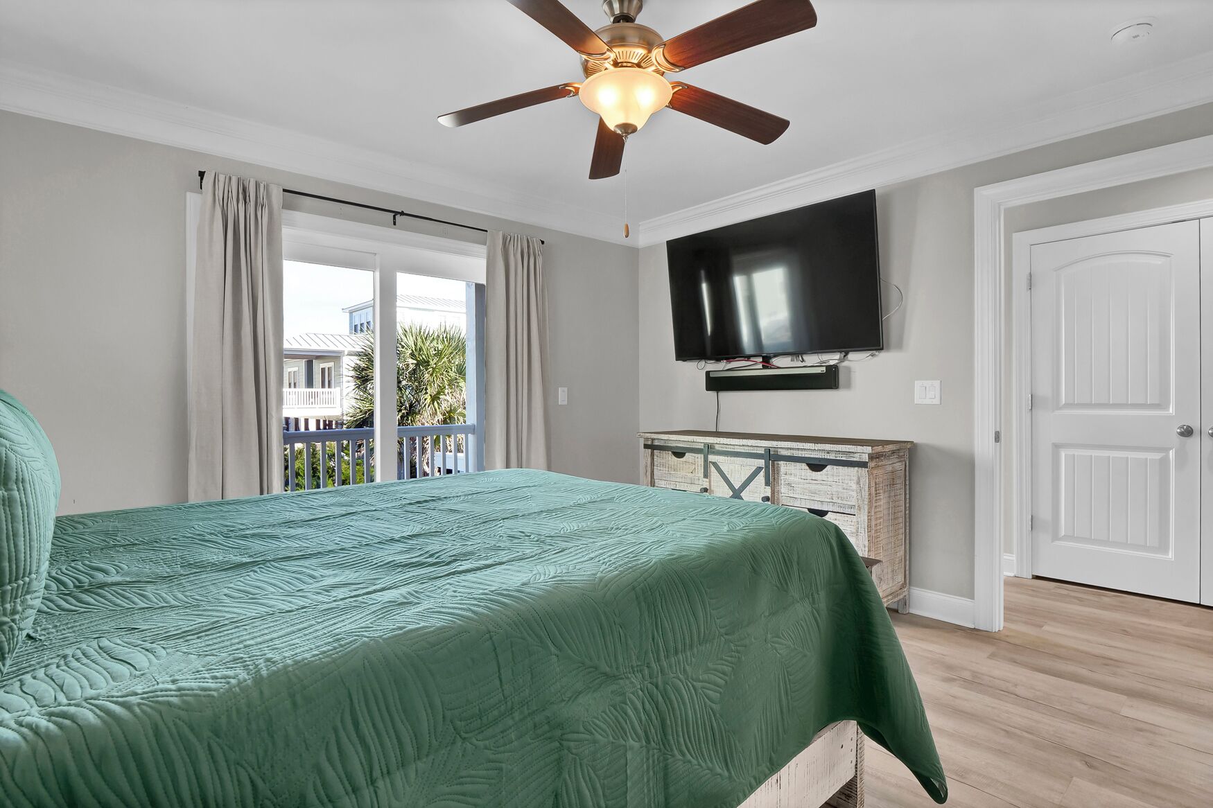 A bedroom with a bed, a ceiling fan, a TV, and a balcony with curtains.