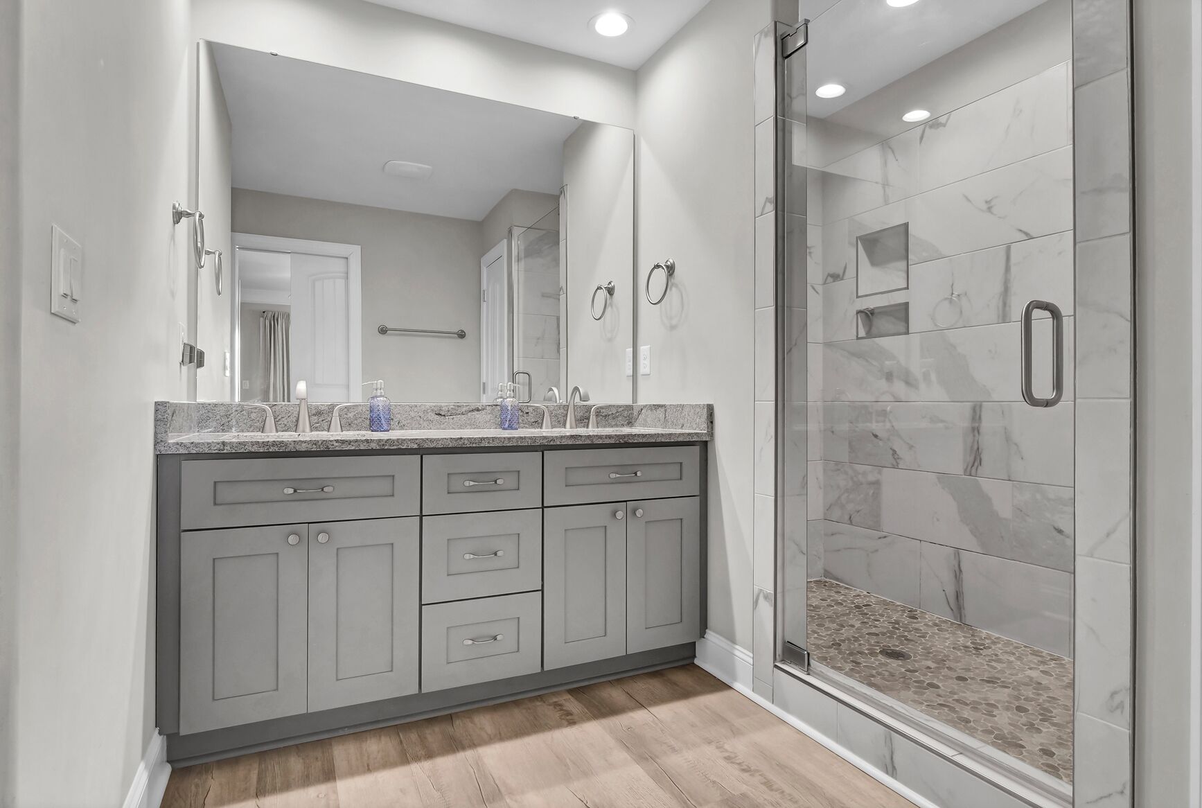 A modern bathroom with a large mirror, a walk-in shower, and a granite countertop.