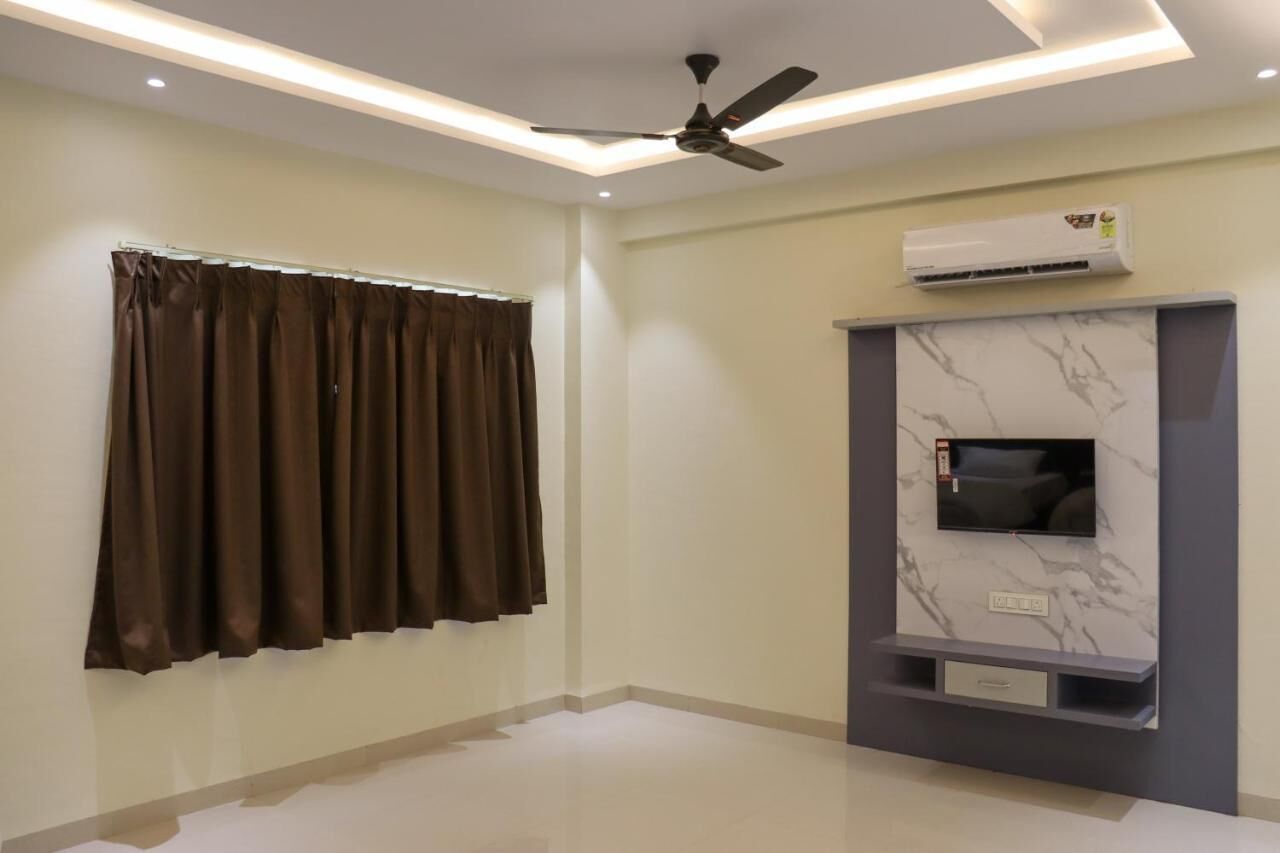 A modern living room with a ceiling fan, a mounted air conditioner, a flat-screen TV on a marble wall, and a window with brown curtains.