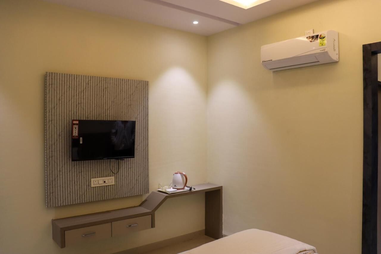 Una camera d'albergo con televisione a schermo piatto montata a parete, una scrivania con lampada e un condizionatore.