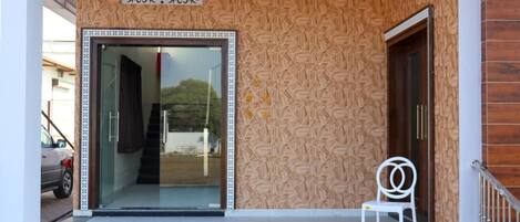 Fachada de un edificio con un muro decorativo, puerta de cristal y una silla blanca.