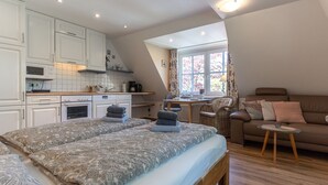 Une chambre compacte comprenant un grand lit, une petite kitchenette, une fenêtre avec des rideaux et un canapé avec une table.