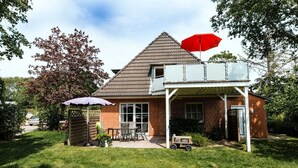 Une maison à deux étages avec un patio couvert, un parasol rouge et un petit jardin.