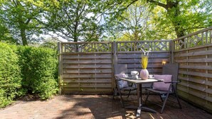 Un espace patio aménagé avec une table et des chaises, un vase décoratif et une clôture en bois.