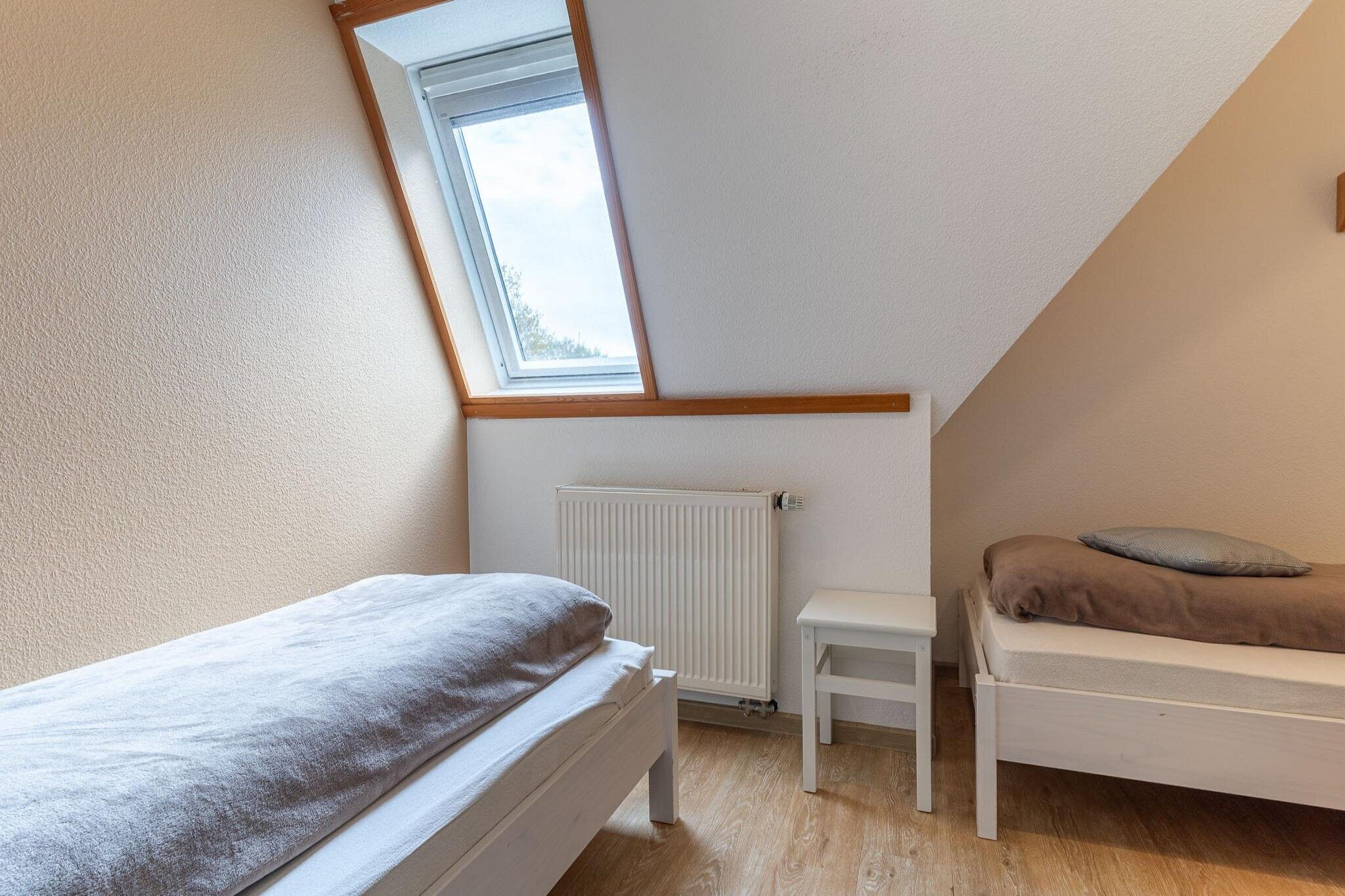 A small, well-lit attic bedroom with a sloped ceiling, a radiator, a window, and two beds.