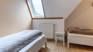 Pieni, hyvin valaistu ullakkohuone, jossa on kalteva katto, patteri, ikkuna ja kaksi sänkyä.