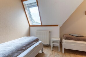 Une petite chambre mansardée, bien éclairée, avec un plafond en pente, un radiateur, une fenêtre et deux lits.