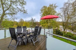 Une terrasse avec une table et des chaises, un parasol rouge, et une vue sur des arbres et un bâtiment en arrière-plan.