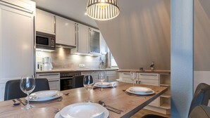 Moderni keittiö, jossa on ruokapöytä neljälle hengelle. Keittiössä on kahvinkeitin, viinilaseja ja lautasia.