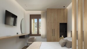 A modern bedroom with a bed, a desk, a chair, and a TV mounted on the wall.