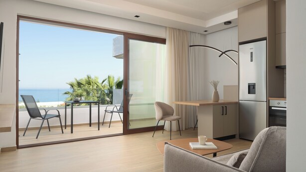 A modern hotel room with a balcony, a dining area, and a kitchenette.
