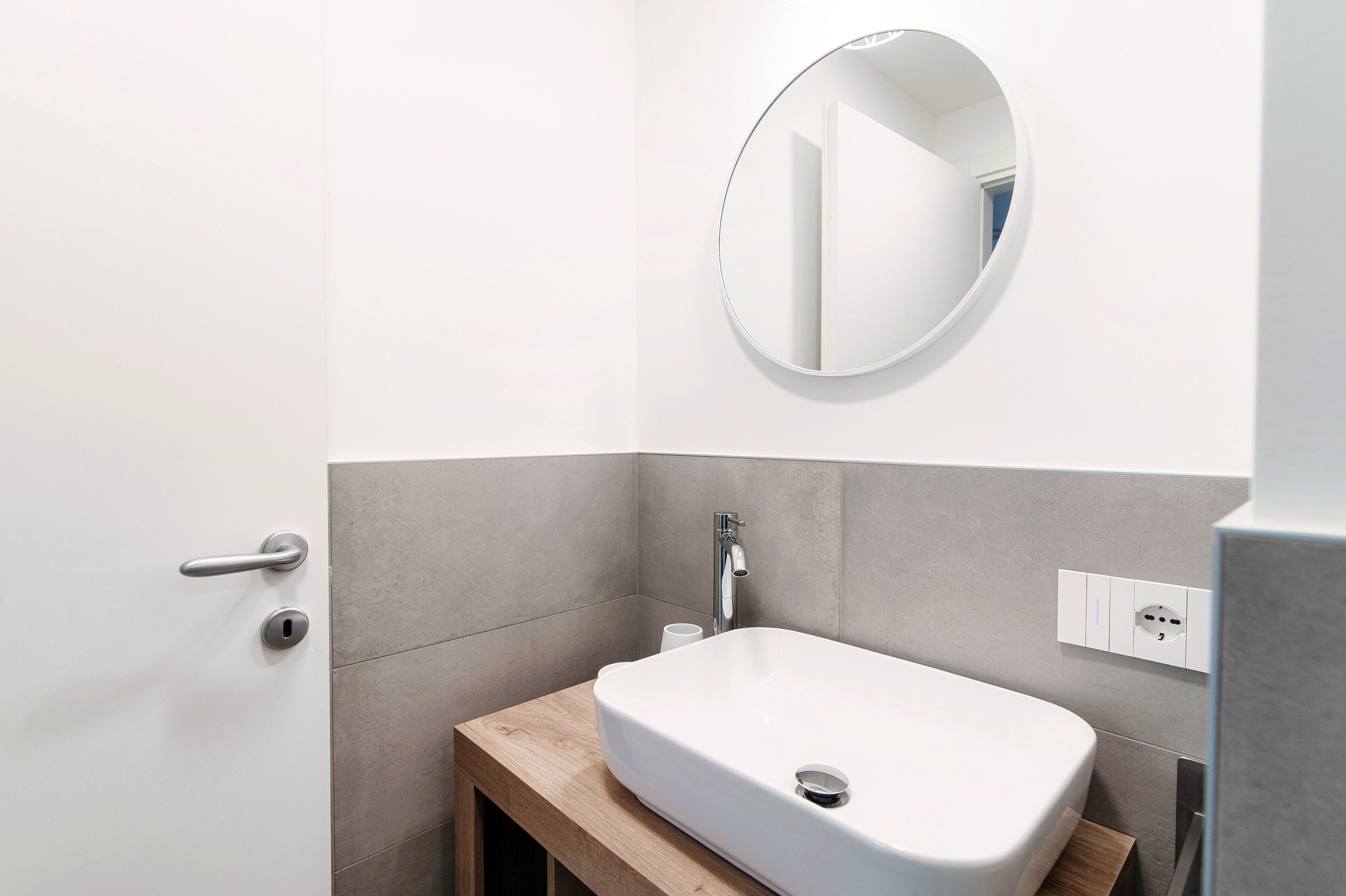 Ein modernes Badezimmer mit Waschbecken, rundem Spiegel und Holzwaschtisch.