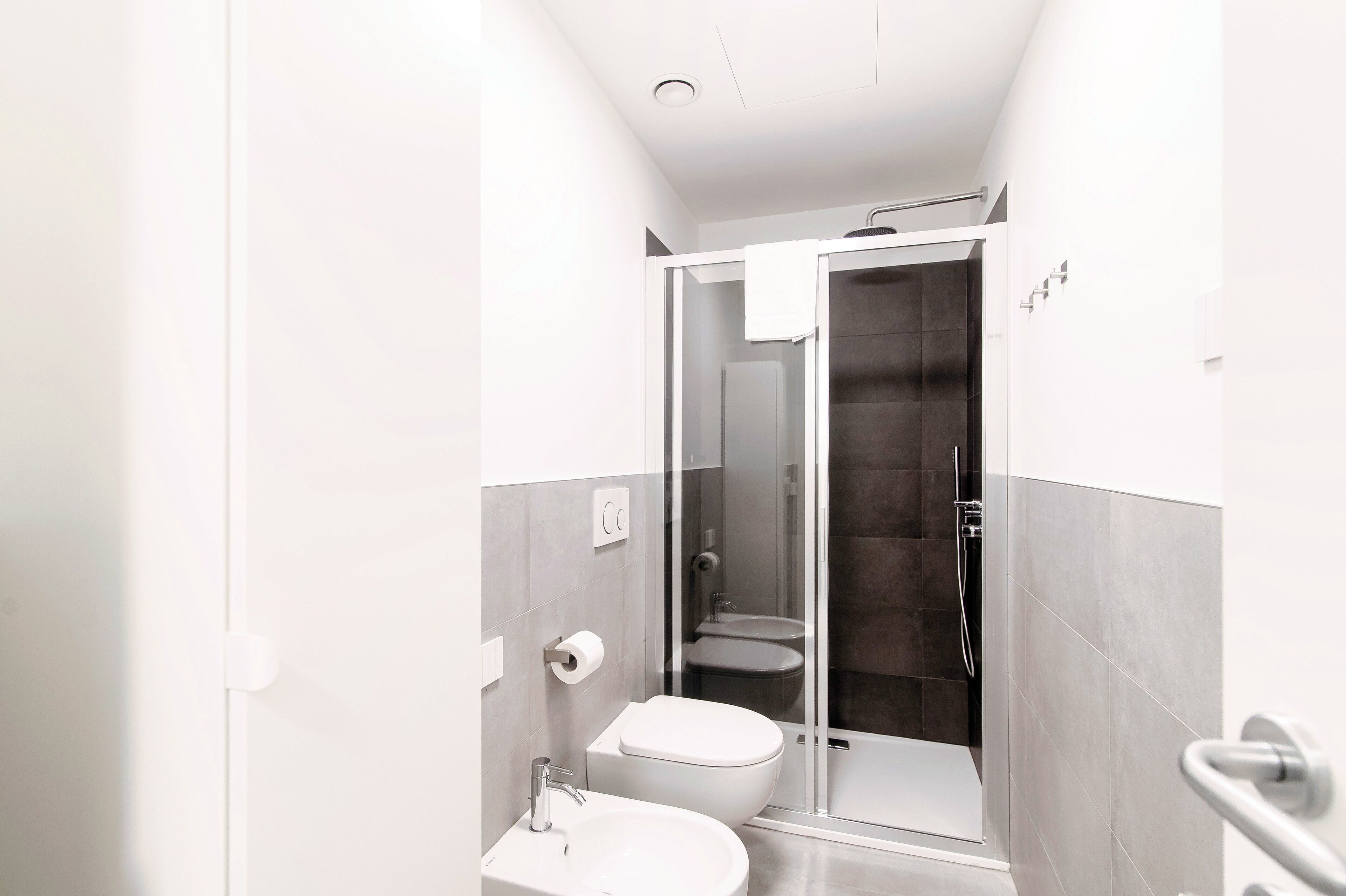 Un baño moderno con inodoro, lavamanos y zona de ducha con mampara de vidrio.