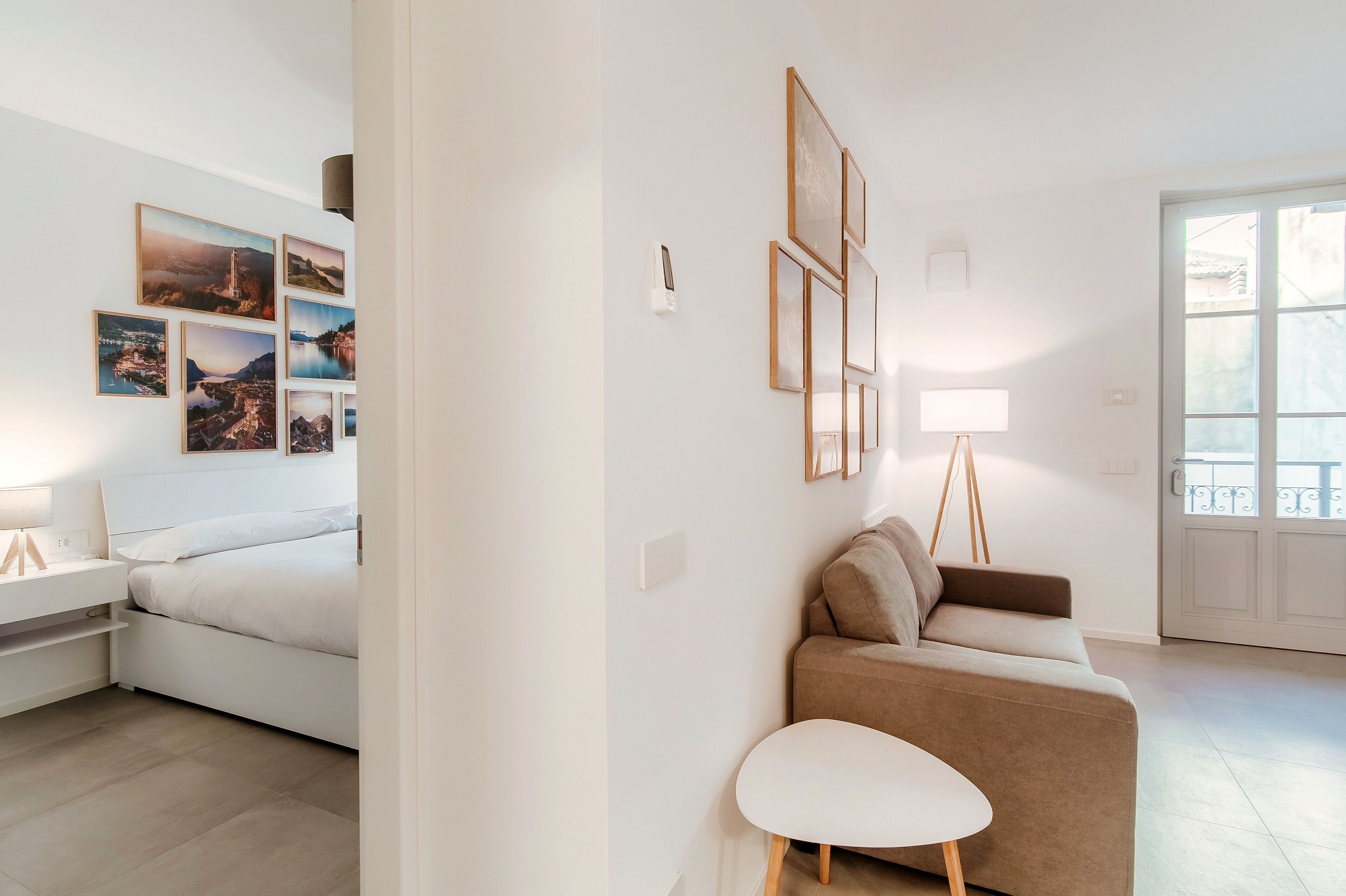 A modern living room with a sofa, a small table, and a bed. There are wall-mounted picture frames and a lamp.