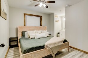 A bedroom with a wooden bed, a ceiling fan, a window with blinds, a bedside table, and a nightstand.