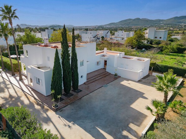 A modern white building with a spacious courtyard, surrounded by greenery and a view of distant hills.