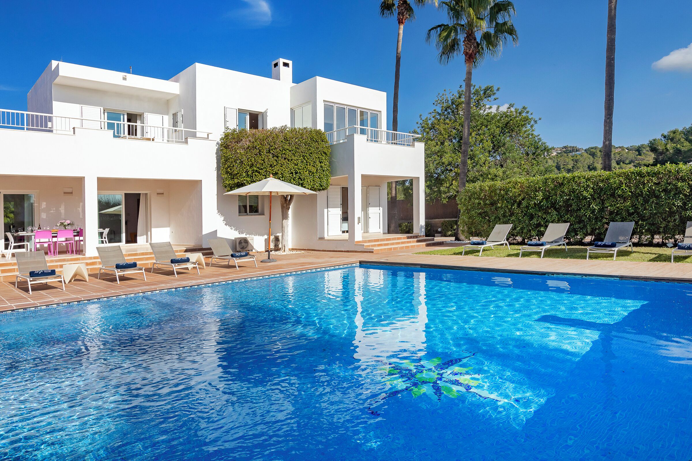 Una casa moderna de dos pisos con piscina, sillas de descanso y vistas a la vegetación circundante.