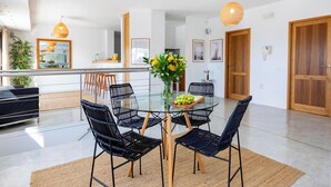 Een moderne eetruimte met een glazen tafel, zwarte geweven stoelen en een centrale vaas met bloemen.