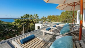 Een houten terras met lounge stoelen en parasols met uitzicht op een zwembad en de oceaan.