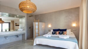 Een moderne slaapkamer met een groot bed, een badkamer met een wastafel en een ladder in de douche.
