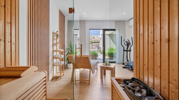 Un intérieur moderne avec un plancher en bois, une porte en verre donnant sur un balcon, un banc en bois, une table avec un verre et une cheminée.