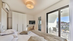 A modern hotel room with a large bed, a desk, a TV, and a balcony with a city view. - Villa Consido, a 3-Bedroom Retreat with sea views (Seget Vranjica)