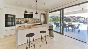 A modern kitchen with a central island, bar stools, and a view of the pool and cityscape through large sliding doors. - Villa Consido, a 3-Bedroom Retreat with sea views (Seget Vranjica)