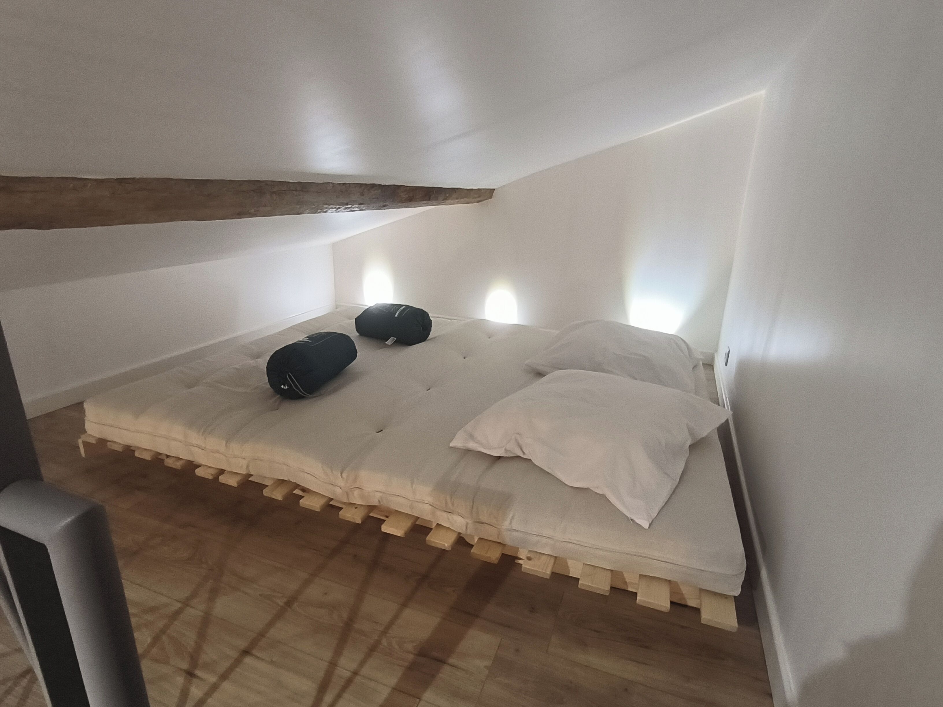A small, narrow attic bedroom with a sloped ceiling, a wooden bed frame, and two pillows.