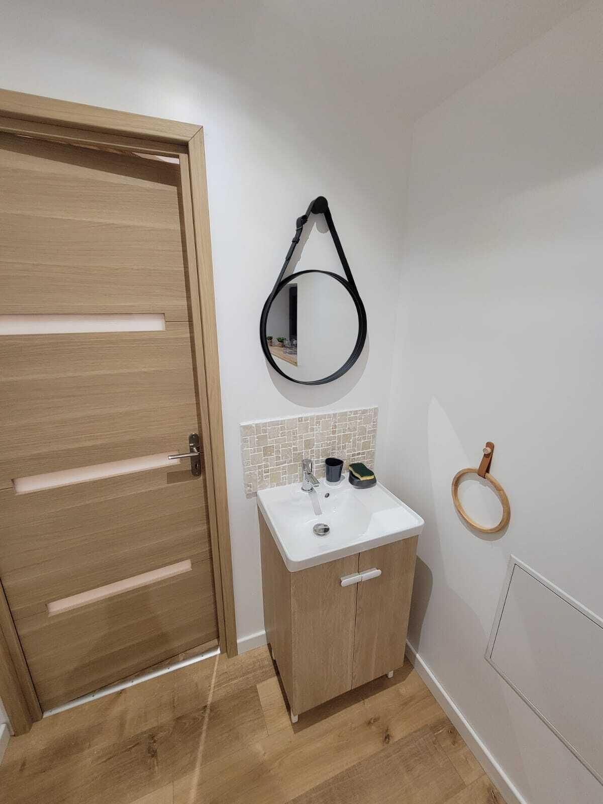 A bathroom with a wooden door, a white sink with a mirror, and a wooden ring on the wall.