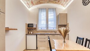 A compact kitchen with a microwave, a small refrigerator, and a dining area with a wooden table and chairs.