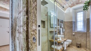 A modern bathroom with a glass-enclosed shower, a large mirror, and a window providing natural light.