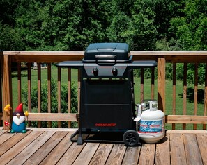 A portable grill with a propane tank on a wooden deck.