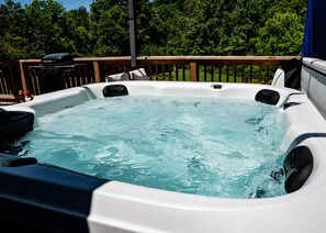 A hot tub with a wooden deck and a grill in the background.