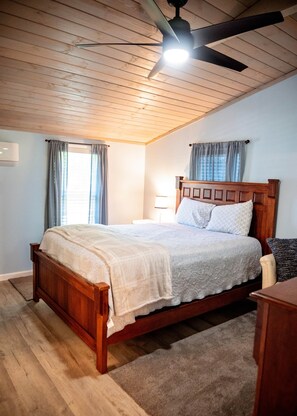 Ein Schlafzimmer mit einem hölzernen Bett, einem Deckenventilator und einem Fenster mit Vorhängen.