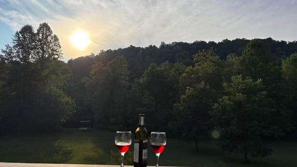 A wooden deck overlooking a lake with a bottle of wine and two glasses.
