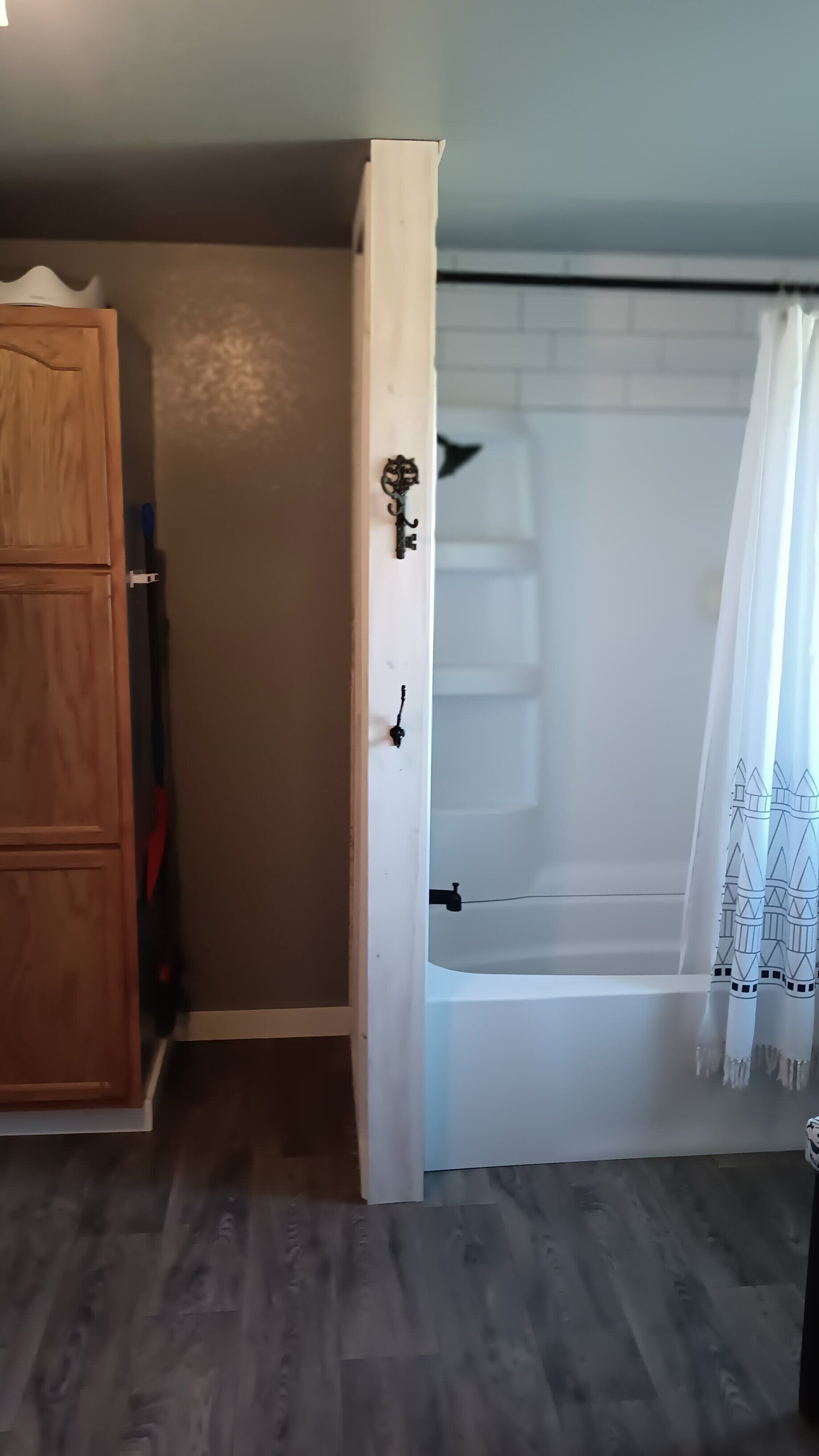 A room with a wooden wardrobe, a white door with a keyhole, and a white bathtub with a shower curtain.