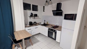 A compact kitchen with white cabinets, a wooden countertop, a black stove, a microwave, and a coffee maker. - T2 au Confort tropical downtown! (Fort-de-France)