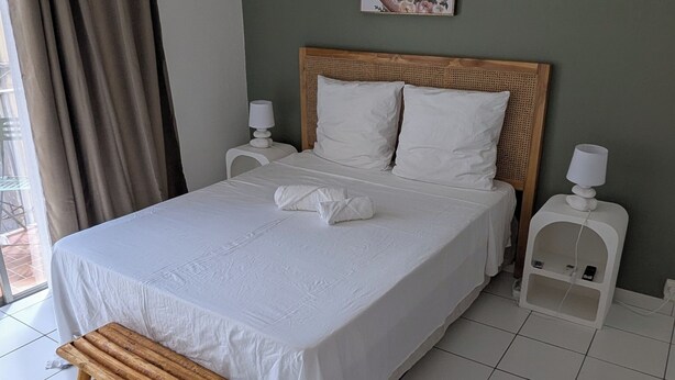 A neatly made bed with white linens, a wooden headboard, and a small wooden stool. - T2 au Confort tropical downtown! (Fort-de-France)