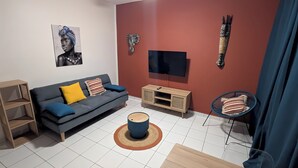 A modern living room with a grey sofa, a wooden TV stand, a blue chair, and a red accent wall. - T2 au Confort tropical downtown! (Fort-de-France)