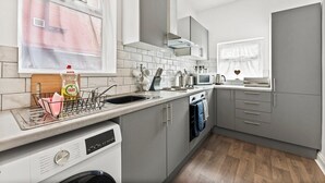 A modern kitchen with grey cabinets, a dishwasher, and a window with a view of a building. - 20% off! Boutique Doncaster Abode - Sleeps 6! (Doncaster)