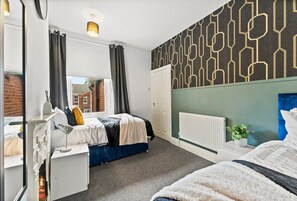 Relax in a stylish bedroom with a large bed, geometric patterned wallpaper, and a window offering a city view.