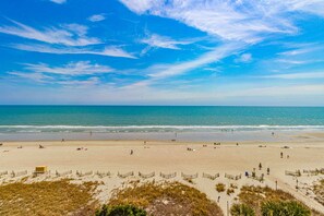 A beach with a clear sky, sandy shore, and a fence in the foreground.